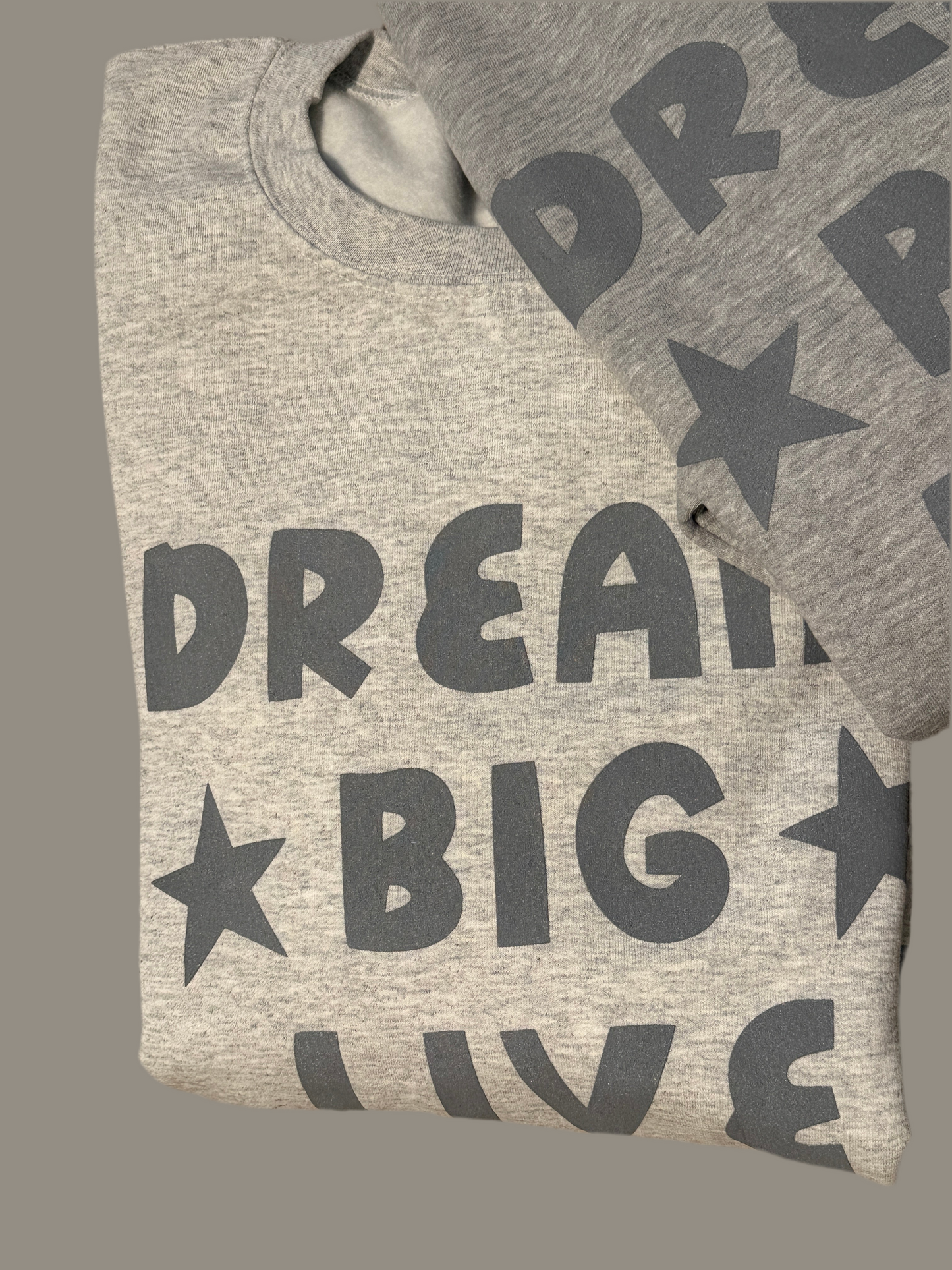 Gray t-shirt with 'Dream Big Live' text and stars on a matching bag against a gray background