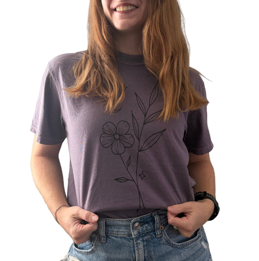 Person wearing a purple t-shirt with a floral design on a plain background