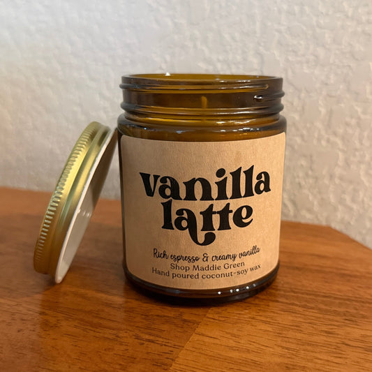 Candle jar labeled 'vanilla latte' on a wooden surface with a white wall background