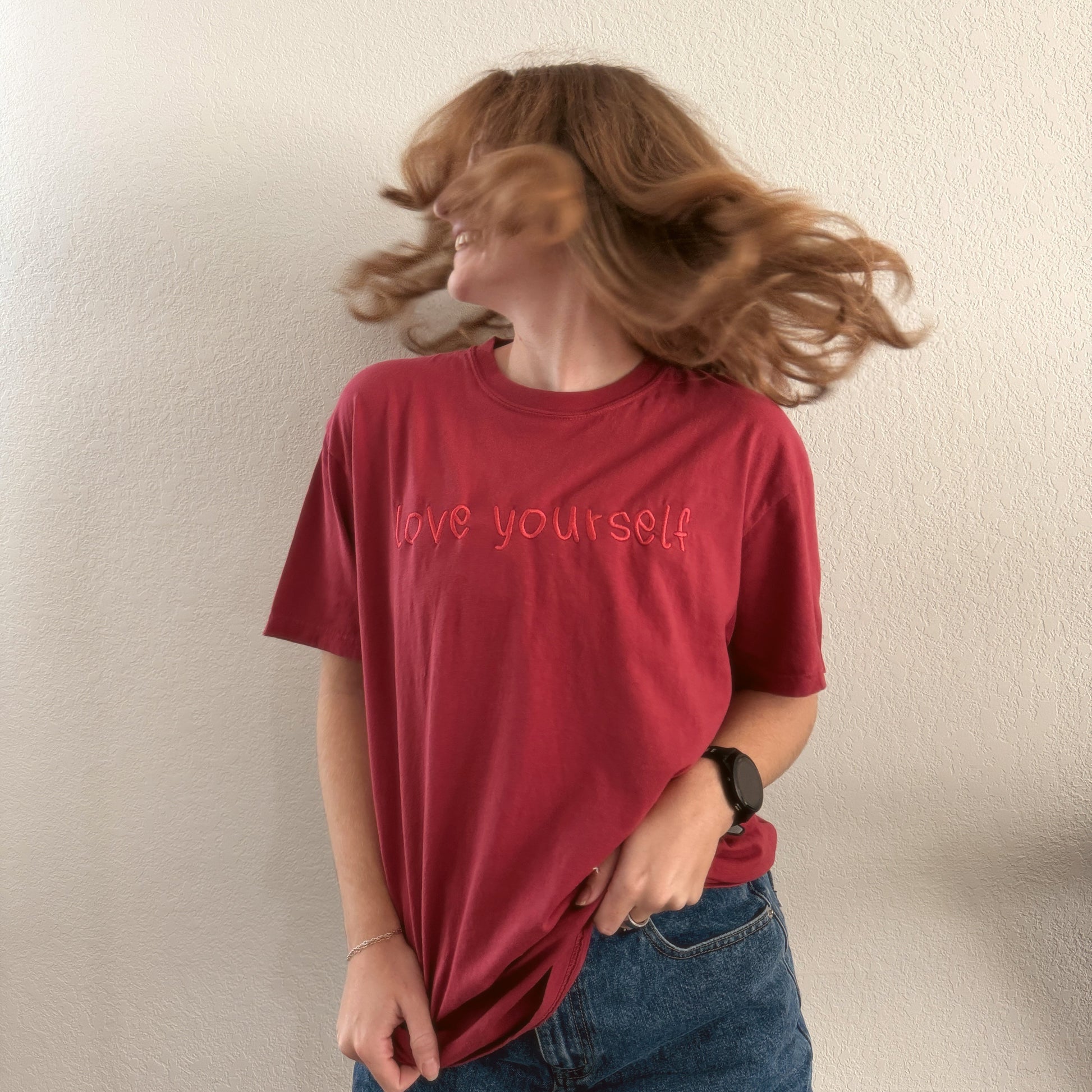 Person wearing a red t-shirt with 'love yourself' text, standing against a plain background